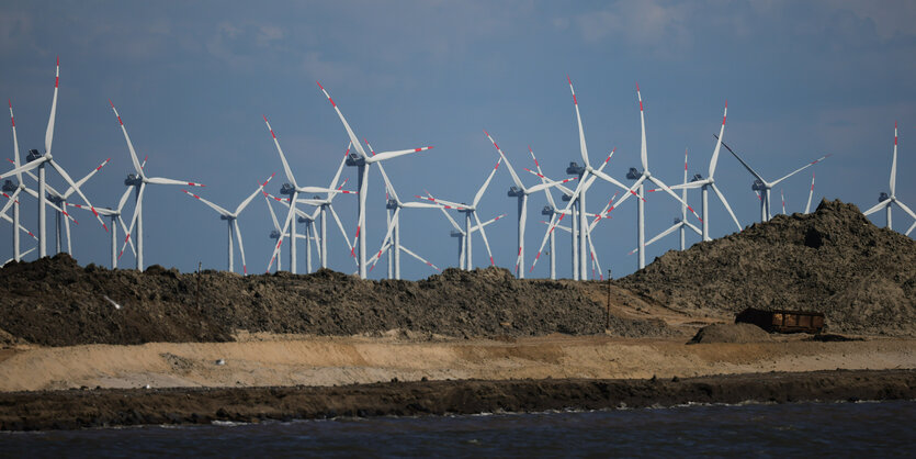 Aufgeschüttete Erdschichten einer Baustelle, dahinter Windkrafträder