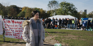 JesidInnen protestieren mit einem Hungerstreif, eine Frau steht vor dem Plakat, im Hintergrund eine Gruppe Männer