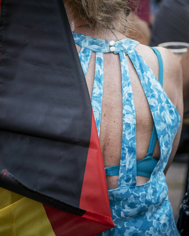 Eine Frau in blauem Oberteil von hinten, daneben eine Deutschlandfahne