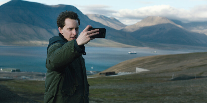 Ein Mann steht vor einem See und macht ein Selfie.