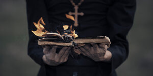 Hände halten eine brennendes Buch , Träger trägt Kreuz