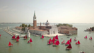 Boote mir roten Segeln auf dem Canal Grande, in der Mitte des Bildes eine bebaute Insel mit kleinem Anlager für Boote