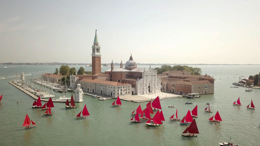 Boote mir roten Segeln auf dem Canal Grande, in der Mitte des Bildes eine bebaute Insel mit kleinem Anlager für Boote