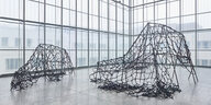 Ausstellungsansicht mit zwei Skulpturen, die aus Gittern bestehen, über die ein Netz aus Stoffen geworfen wurde