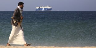 Ein bewaffneter Mann an einem Strand, auf dem meer ist ein Frachtschiff zu sehen