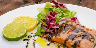 Ein Stück Lachs mit Zitronen Scheiben und Balsamico Dressing auf einem weißen Teller