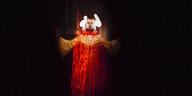 Die Musikerin Mary Ochher trägt leuchtene Widderhhörner und schreitet aus einem dunklen Gang auf die Kamera zu. Ihr Kleid ist komplett mit Wachstropfen überzogen. Sie ist in gelb und rot schimmerndes Licht getaucht.