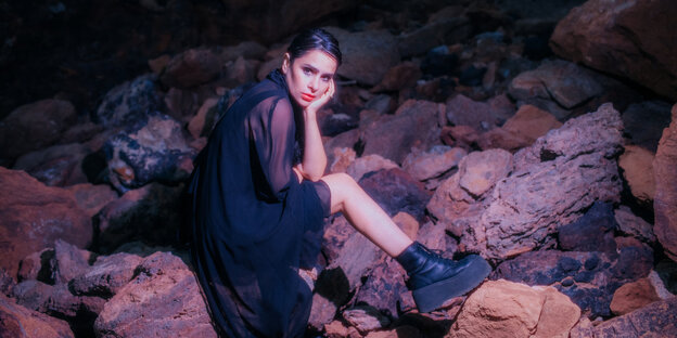 Sofia Kourtesis sitzt im Dunkeln auf Steinen
