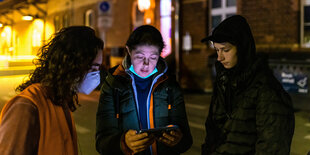 Drei Menschen stehen über ein Smartphone gebeugt an einem Bahnhof