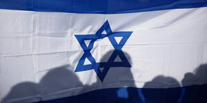 Silhouetten von mehreren Personen, die hinter einer israelischen Fahne stehen