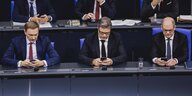 Christian Lindner, Robert Habeck und Olaf Scholz sitzen auf ihren Plätzen im Bundestag und schauen auf ihre Handys