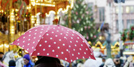 Person mit einem roten Regenschirm auf einem Weihnachtsmarkt.