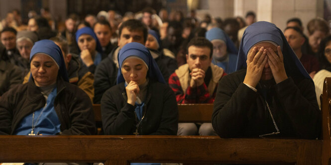 Traurig blickende Menschen bei der Mitternachtsmesse auf Bänken in der Katharinenkirche direkt neben der Geburtskirche in Bethlehem.