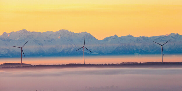 Windäder in Nebel vor Berglandschaft im Sonnenaufgang