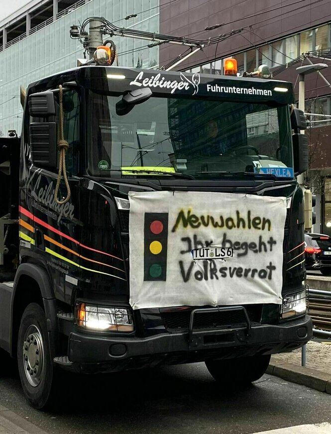 Am Kühlergrill eines Lastwagens ist ein Transparent befestigt auf dem eine Ampel gemalt ist mit der Forderung: Neuwahlen, ihr begeht Volksverrat