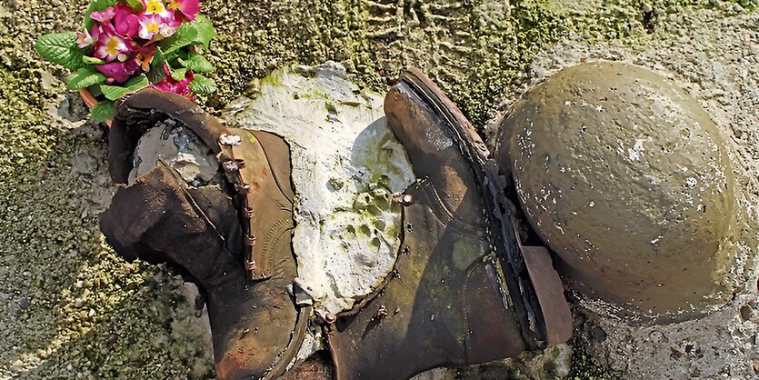 Eine Blume, ein paar Soldatenstiefel und ein Helm liegen nebeneinander auf dem Boden