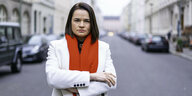 Swetlana Tichanowskaja steht mitten auf einer Straße, weißer Mantel, roter Schal, verschränkte Arme und entschlossener Blick direkt in die Kamera