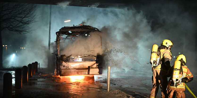 Feuerwehrleute löschen in der Silvesternacht 2022/23 in Neukölln einen in Brand gesetzten Bus