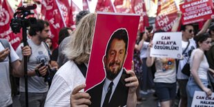 Eine Frau hält sich eon Plakat mit einem Foto von Can Atalay vor ihr Gesicht