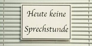 Ein Schild mit der Aufschrift: "Heute keine Sprechstunde" hängt vor einem geschlossenen Rollladen