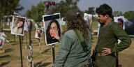 Soldatin und ein Soldat schauen sich ein Foto einer Frau an, das im Freien ausgestellt ist. Die Soldatin berührt das Gesicht auf dem Bild. Im Hintergrund weitere Fotografien