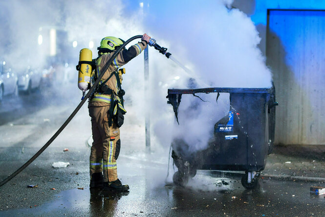 ein Feuerwehrmann löscht eine brennende Mülltonne