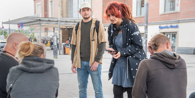 Sozialarbeiterin Mira Arwan spricht vor dem Kieler Hauptbahnhof mit Menschen, die vor ihr auf der Straße sitzen