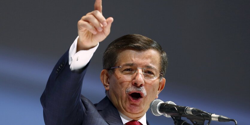 Ahmet Davutoglu mit erhobener Hand an einem Mikrofon.