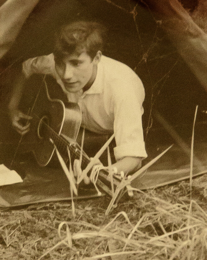 Ein altes Bild von Hedo Holland, auf dem er Gitarre spielt und im Stroh sitzt.