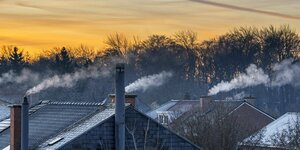 Rauchende Schornsteine auf verschneiten Dächern bei Sonnenaufgang.
