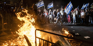 Viele Menschen protestieren mit israelischen Flaggen. Barrieren brennen im Vordergrund.