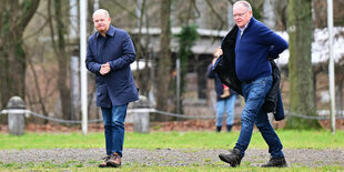 Olaf Scholz und Stefan Weil, der sich im Gehen eine Jacke anzieht, auf einer matschigen Wiese