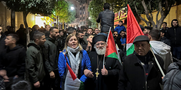 PalästinenserInnen protestieren in Ramallah, ein Geistlicher und ein Mann tragen palästinensiche Flaggen über der Schulter