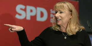 Eine blonde Frau zeigt mit dem Finger nach links.