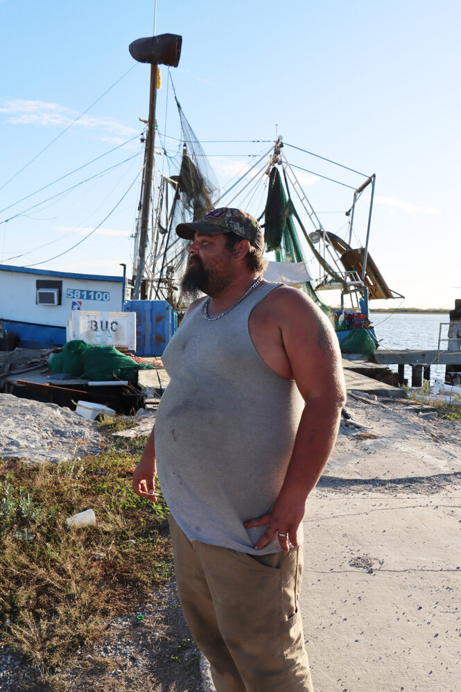 Travis Dardar steht im Hafen vor kleinen Booten und raucht eine Zigarette