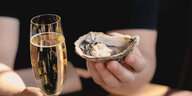 Champagnerglas und eine Hand, die eine Auster hält.