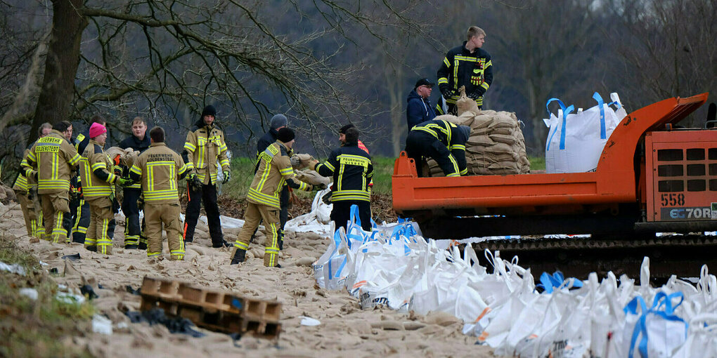 Feuerwehrleute sichern einen Deich mit Sandsäcken.