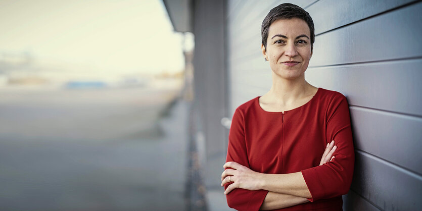 Eine junge Frau im roten Pullover steht vor einer Hauswand.