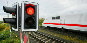 Eine rote Ampel leuchtet an einem Bahnübergang als ein ICE der Deutschen Bahn vorbeifährt.