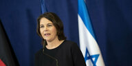 Außenministerin Baerbock steht an einem Pult, hinter ihr die Flagge Israels