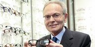 Günther Fielmann hält eine Brille vor einem Brillenregal