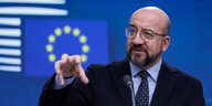 Ein Mann steht vor einem EU-Logo und gestikuliert mit der rechten Hand