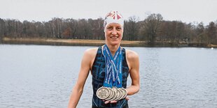 Eisschwimmerin Tina Deeken steht vor einem Gewässer und zeigt ihre Medaillen.