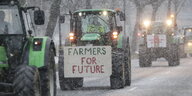 Traktoren fahren bei Schneefall bei einer Demonstration von Bauern über eine Straße. Auf einem Traktor haben Landwirte dabei ein Schild mit der Aufschrift "Farmers For Future" befestigt. Als Reaktion auf die Sparpläne der Bundesregierung hat der Bauernverband zu einer Aktionswoche mit Kundgebungen und Sternfahrten ab dem 8. Januar aufgerufen.