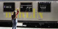 Eine Frau steht winkend vor einem Zug, der die Aufschrift "Berlin" trägt