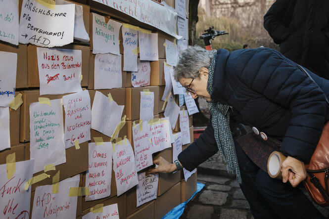 Eine ältere Dame bringt einen Zettel an der "Brandmauer gegen Rechts" an.