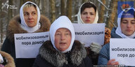 Frauen mit weißen Kopdtüchern halten weiße Schilder mit kyrillischer Schrift