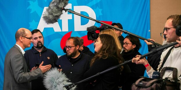 Journalisten und Journalistinnen diskutieren mit Stefan Möller, Co-Landessprecher der AfD, (links) und halten ihm ihre Mikrofone entgegen