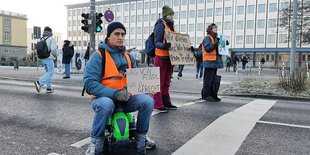 Ein Mann mit Warnweste sitzt auf einem Spielzeugtrecker und blockiert mit zwei anderen Personen eine Straße.