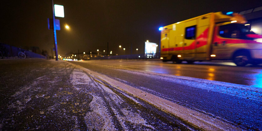 Krankenwagen fährt mit Blaulicht über eine mit Glatteis überzogene Straße